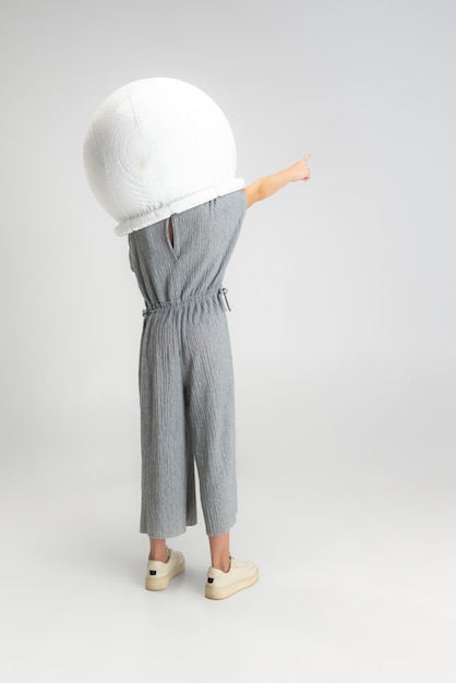 Retrato de una niña caucásica de escuela pequeña con un casco grande posando aislada sobre un estudio blanco