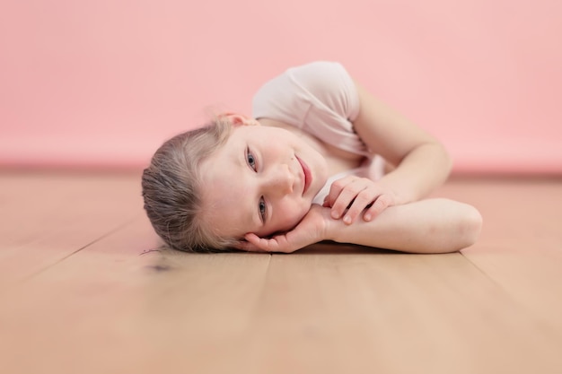 Retrato de una niña caucásica sonriente y feliz tendida en el parquet sobre fondo rosa