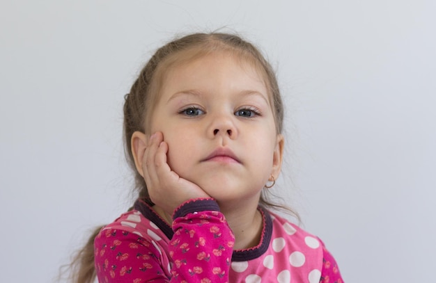 Retrato de una niña caucásica de tres años sosteniendo su barbilla con la mano con cara seria y mirando la cámara en el fondo blanco