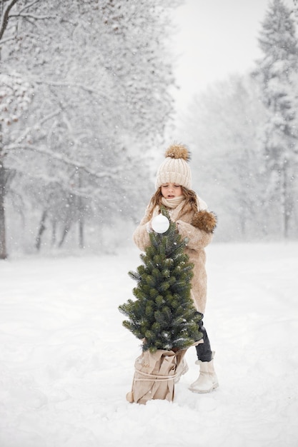 Retrato de niña cerca de un árbol de Navidad en una olla en el bosque en el día de invierno