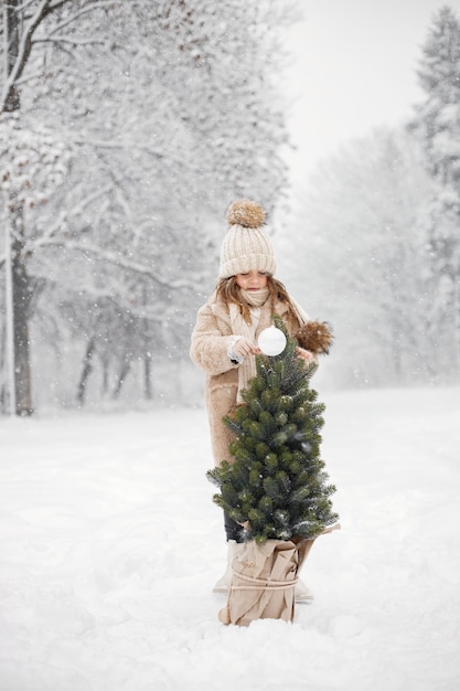 Retrato de niña cerca de un árbol de Navidad en una olla en el bosque en el día de invierno