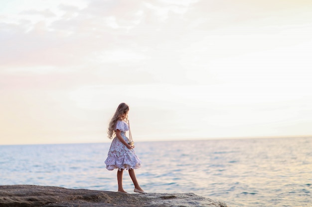 Retrato de una niña cerca del mar sentado en las rocas con un barco de juguete en las manos