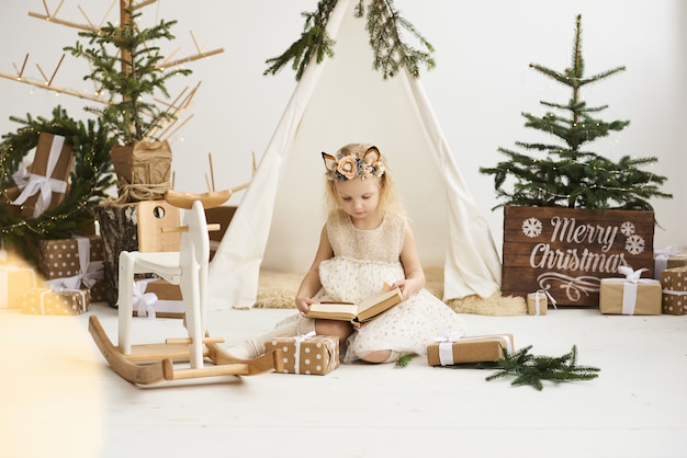 Un retrato de una niña cerca de la tienda india y el árbol de Navidad desempacar regalos de Navidad sobre un fondo blanco.
