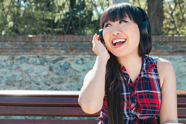 Retrato de niña china atractiva en el fondo urbano escuchando música con auriculares