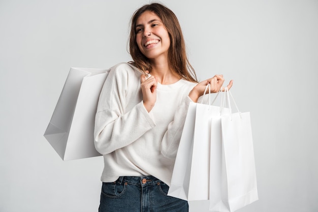 Retrato de niña compradora llena de alegría con ropa elegante levantando bolsas y sonriendo con felicidad, sorprendida y emocionada por las compras en la tienda de moda, venta de segunda mano. Foto de estudio aislado sobre fondo blanco.