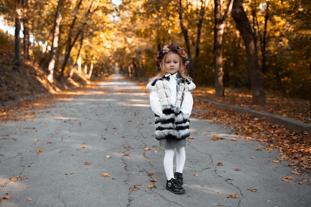 Retrato de niña con corona de flores en la cabeza en el fondo del parque dorado en el día de otoño