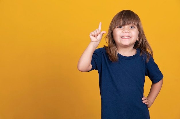 Retrato de niña con el dedo apuntando hacia arriba Niño pequeño en pose tiene idea aislada en pizarra amarilla Éxito idea brillante ideas creativas y concepto de tecnología de innovación