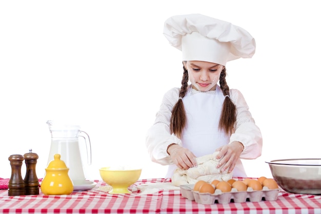 Retrato de una niña en un delantal blanco y un sombrero de chef amasar la masa en la cocina