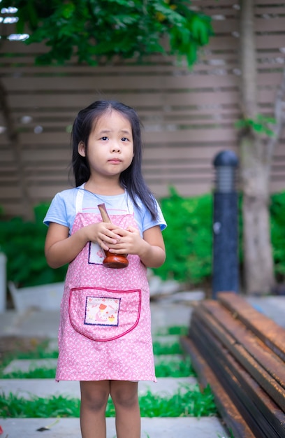 Retrato de niña en delantal con mortero en el jardín