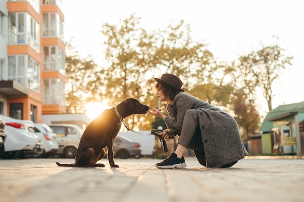 Retrato de niña dueña y hermoso perro con correa sentado en la calle