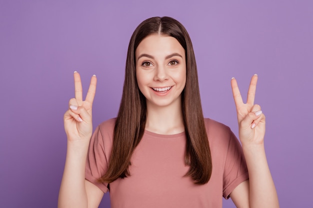 Retrato de niña emocionada positiva gesticulando dos signos v aislados sobre fondo violeta