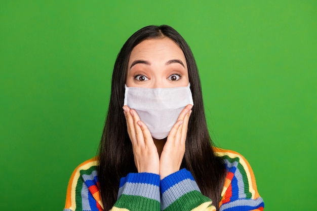 Retrato de niña encantadora bastante asombrada manos mejillas usar máscara médica facial aislada sobre fondo de color verde