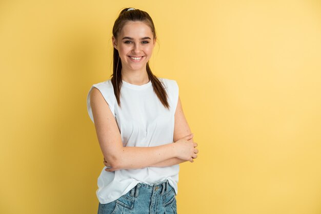 Retrato de una niña encantadora en una camiseta blanca y pantalones vaqueros azules sobre un fondo de una pared amarilla en blanco.