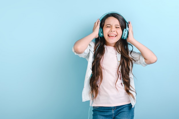 Retrato de una niña encantadora con los ojos cerrados en los auriculares escuchando música y cantando toca su cabeza