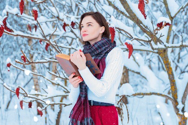 Retrato de una niña encantadora que lee un libro en el bosque de invierno.