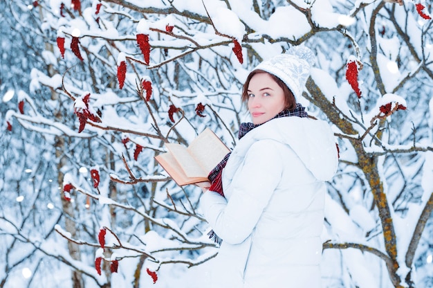 Retrato de una niña encantadora que lee un libro en el bosque de invierno.