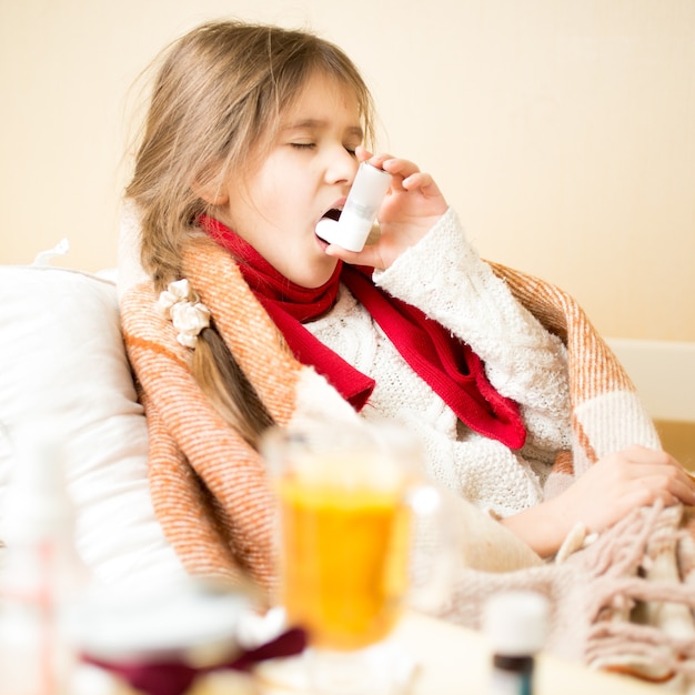 Retrato de niña enferma con enfermedad respiratoria acostada en la cama y con inhalador