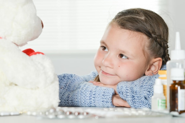 Retrato de una niña enferma con oso de peluche blanco en casa