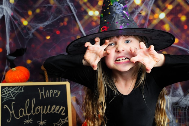 Retrato de una niña enojada con un disfraz de bruja en el fondo de Halloween