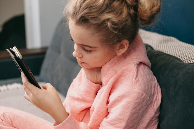 Retrato de una niña escribiendo un mensaje corto en el teléfono móvil sentado en el sofá en el interior hermoso portr