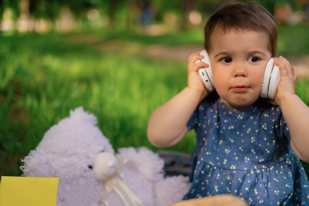 Retrato de una niña escuchando música con auriculares modernos en un parque al aire libre Niño feliz