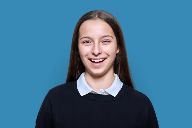Retrato de niña estudiante adolescente alegre mirando a la cámara sobre fondo de estudio de color azul Sonriente atractivo adolescente positivo felicidad escuela secundaria adolescencia juventud concepto