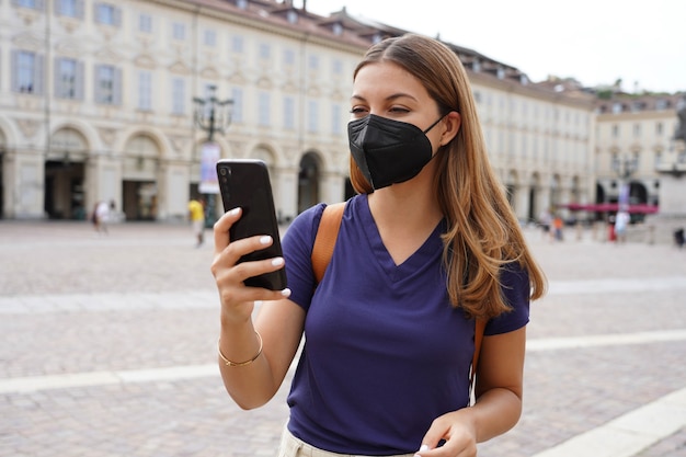 Retrato de niña estudiante con máscara protectora negra FFP2 KN95 con teléfono inteligente al aire libre