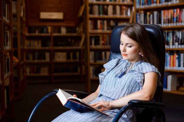 Retrato de una niña estudiante sentada en un cómodo sillón y leyendo un libro