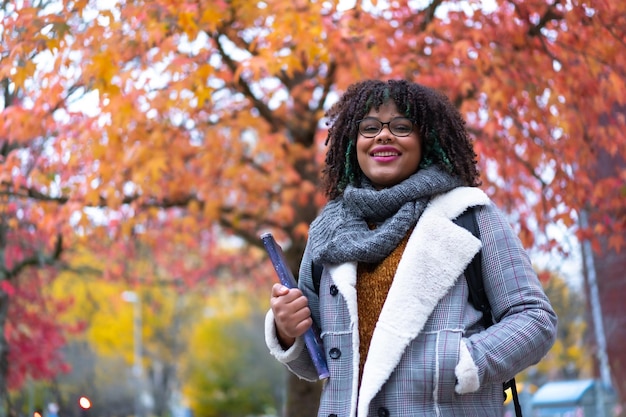 Retrato de niña étnica negra paseando en la universidad bajo árboles de follaje de otoño en el regreso a la escuela