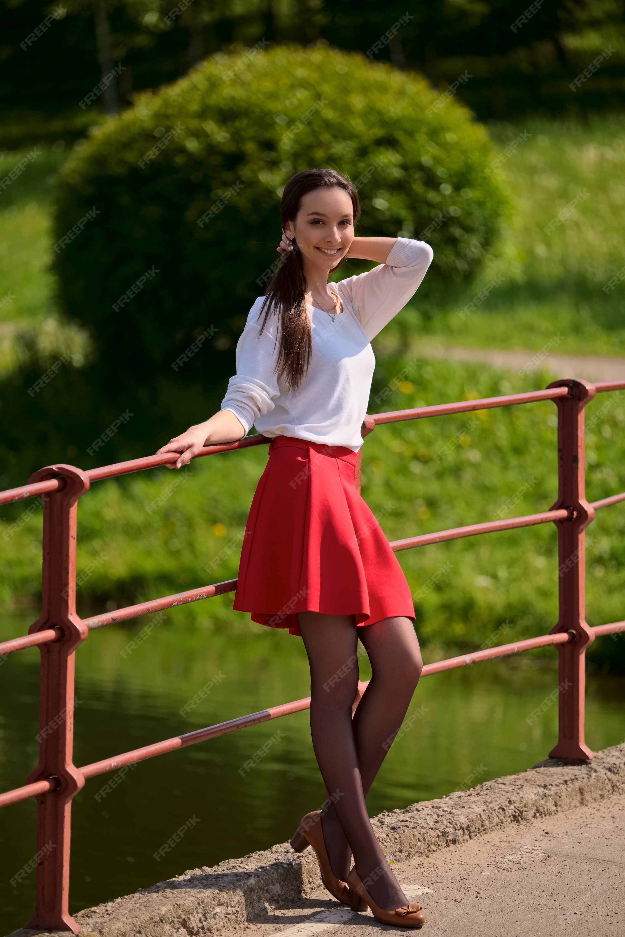 Retrato de una niña en falda roja y blusa blanca apoyada contra una baranda del en la orilla del río | Foto