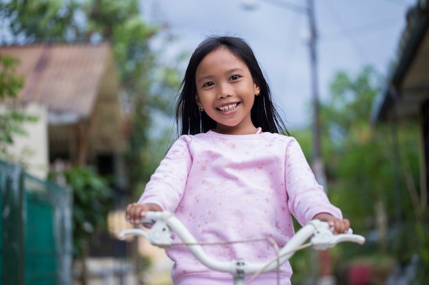 Retrato de una niña feliz alegre niño asiático en bicicleta