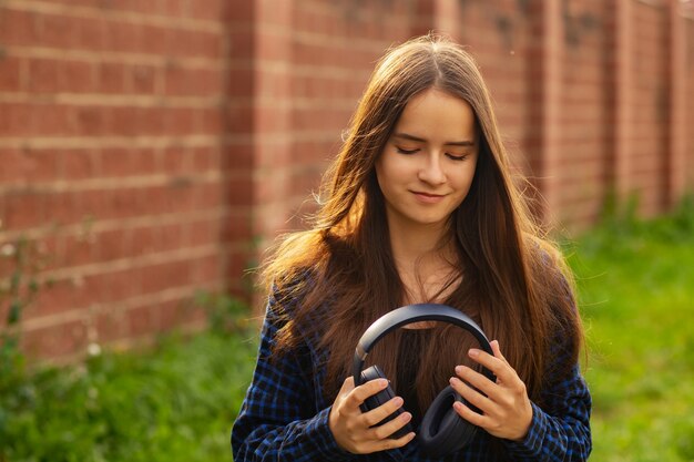 Retrato de una niña feliz en auriculares inalámbricos en verano en una calle de la ciudad en un día soleado