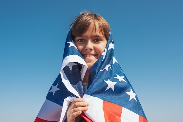 Retrato de niña feliz con bandera americana al aire libre sobre fondo de cielo azul