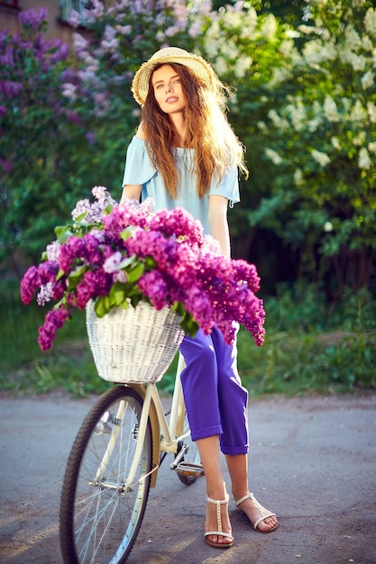 Retrato de una niña feliz con bicicleta vintage y flores en el fondo de la ciudad en la luz del sol al aire libre.