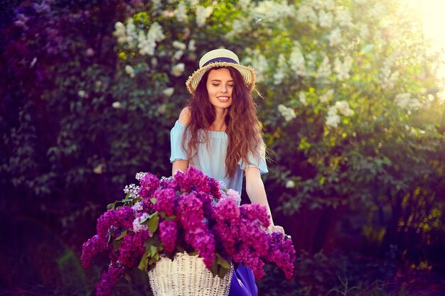 Retrato de una niña feliz con bicicleta vintage y flores en el fondo de la ciudad en la luz del sol al aire libre.