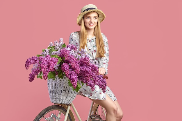 Retrato de una niña feliz con bicicleta vintage y flores sobre fondo rosa.