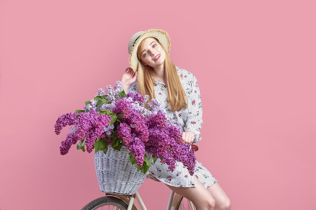 Retrato de una niña feliz con bicicleta vintage y flores sobre fondo rosa.