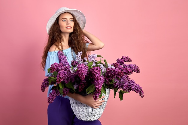 Retrato de una niña feliz con canasta llena de lilas sobre fondo rosa.