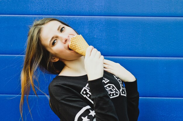 Retrato de niña feliz comiendo helado, al aire libre, sobre fondo de pared azul