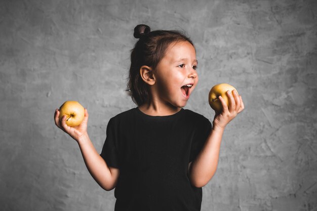 Retrato de una niña feliz comiendo una manzana verde sobre gris