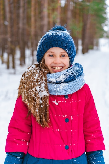 Retrato de una niña feliz en invierno con un sombrero cubierto de nieve que camina en el bosque de invierno