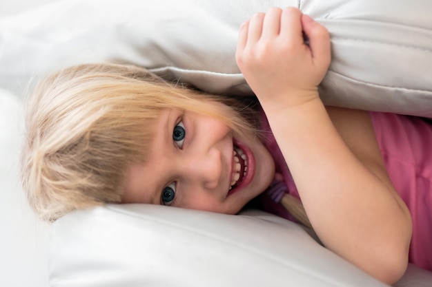 Retrato de niña feliz jugando con almohadas en la cama