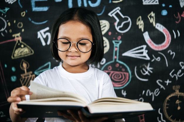 Retrato niña feliz leyendo libros de texto con pizarra