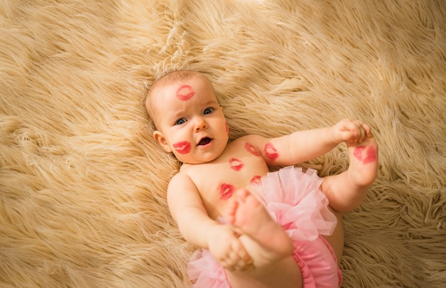 Retrato de una niña feliz con muchos besos rojos en su cuerpo acostado sobre una manta beige mullida