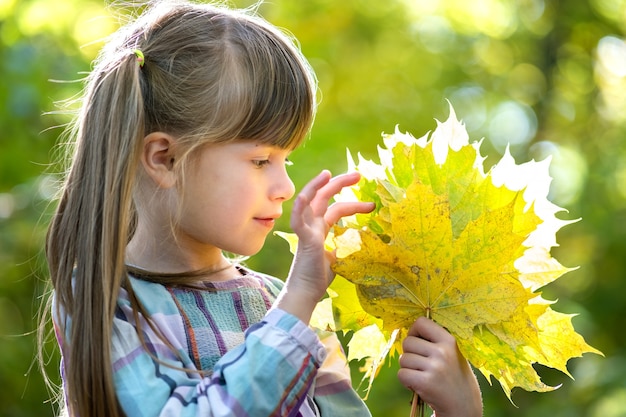 Retrato de niña feliz niño bonito sosteniendo un montón de hojas de árboles caídos en el bosque de otoño