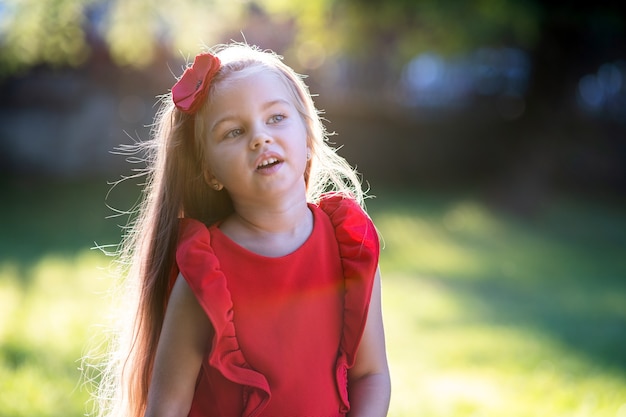 Retrato de niña feliz niño bonito en vestido rojo sonriendo al aire libre disfrutando de un cálido día de verano soleado.
