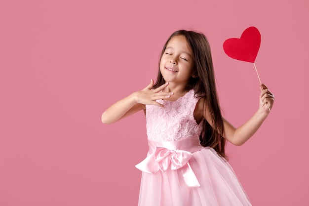 Retrato de niña feliz niño lindo en un vestido rosa con corazón de papel