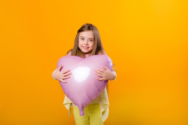 Retrato de una niña feliz niño sonriente sosteniendo un globo rosa en forma de corazón