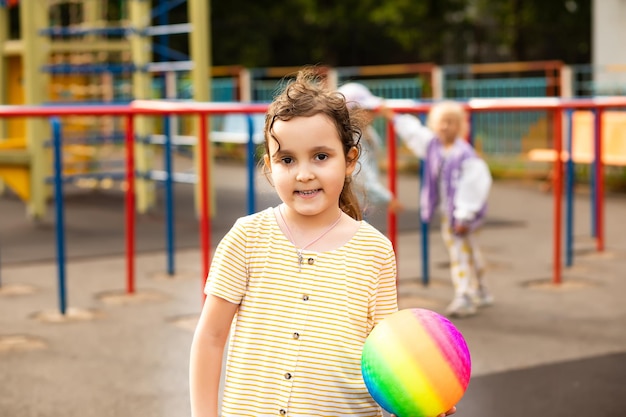 Retrato de una niña feliz en el parque infantil con una colorida bola de arco iris Actividad infantil de verano