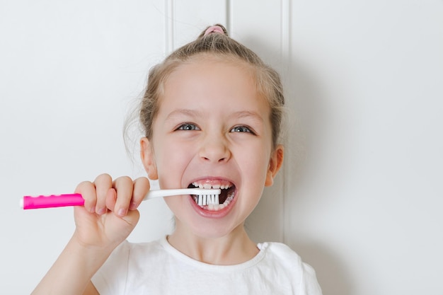 Retrato de una niña feliz que se cepilla los dientes con un cepillo de dientes rosa Fondo blanco